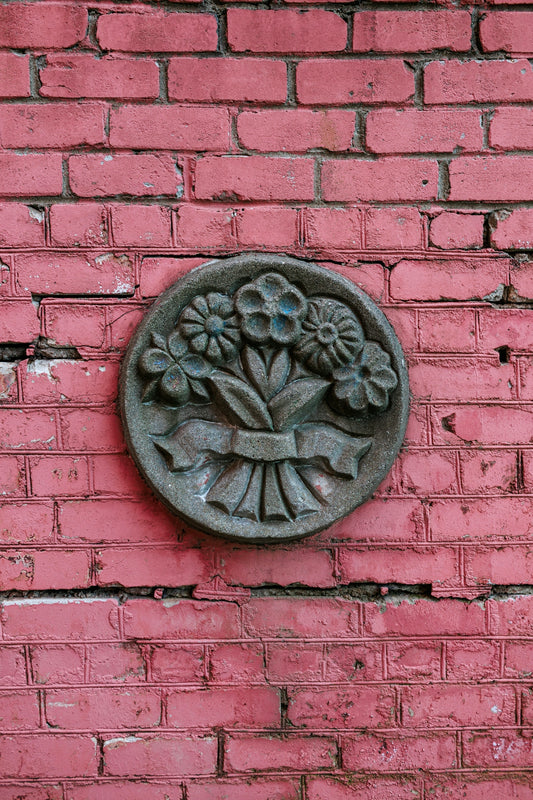 Circular floral relief mounted on pink brick wall