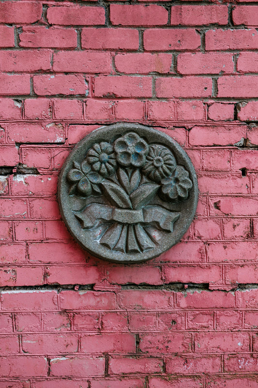 Circular floral relief mounted on pink brick wall