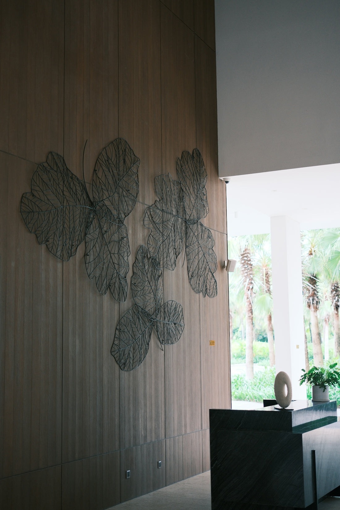 Wire leaf art adorns wooden wall above reception desk