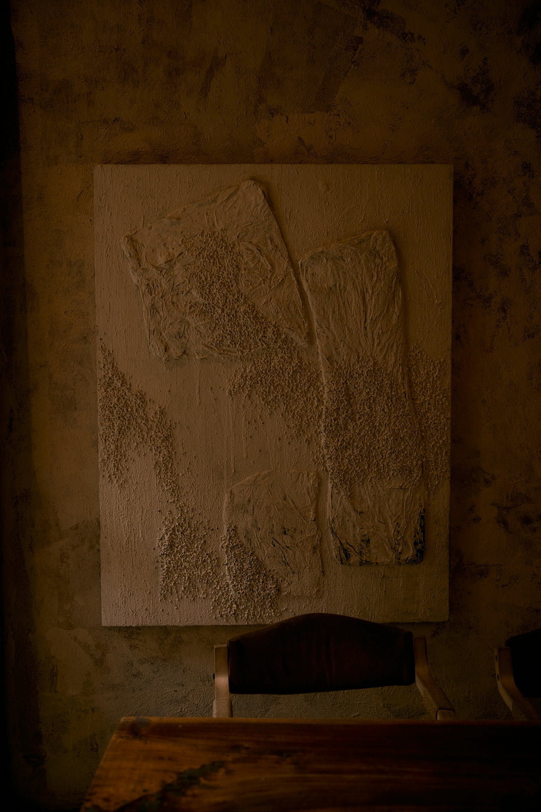 Textured abstract art on a wall above a wooden table.
