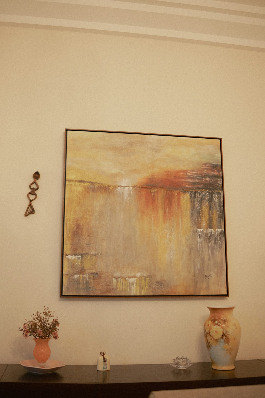 Abstract painting with warm colors above a vase.