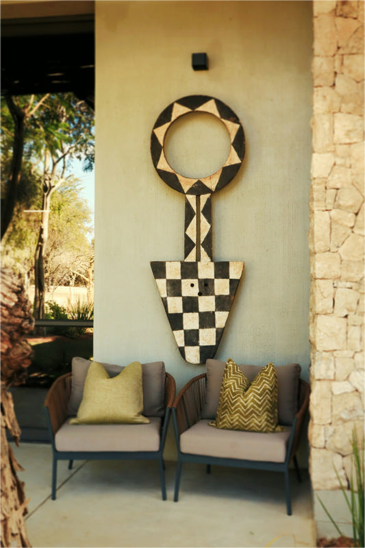 Two outdoor chairs below a large, patterned wooden wall art.