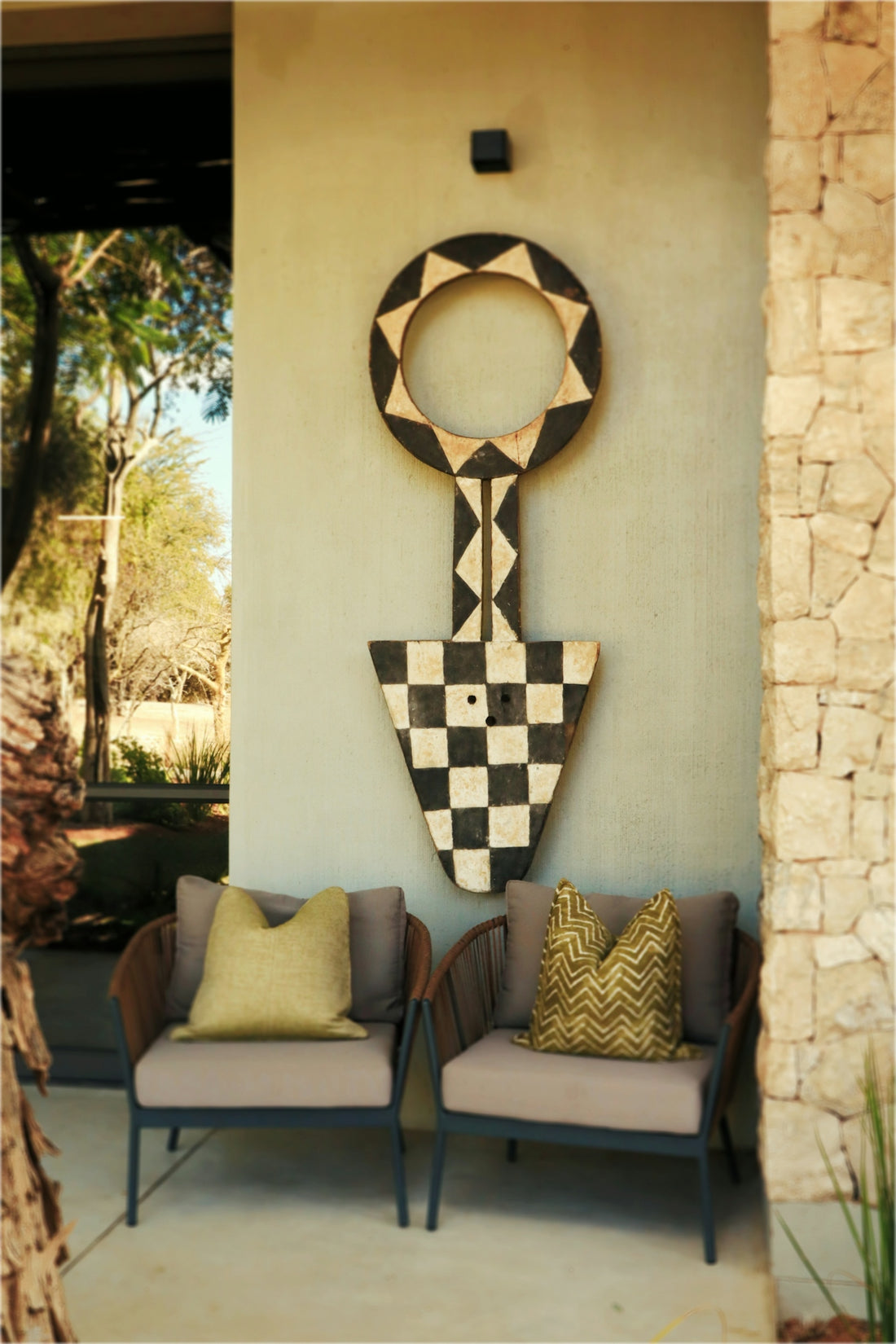 Two outdoor chairs below a large, patterned wooden wall art.
