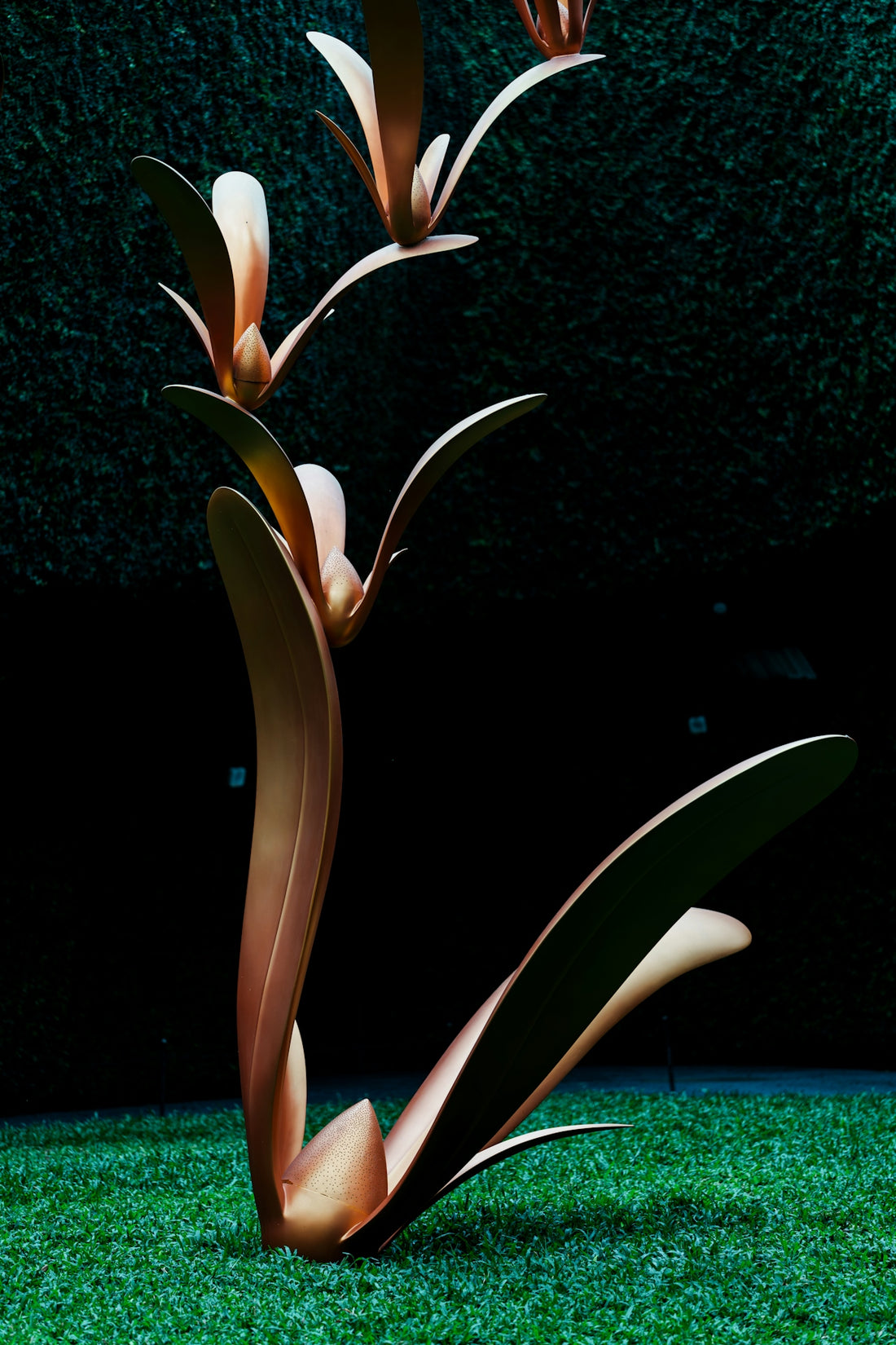 Metallic plant-like sculpture on green grass against a dark background