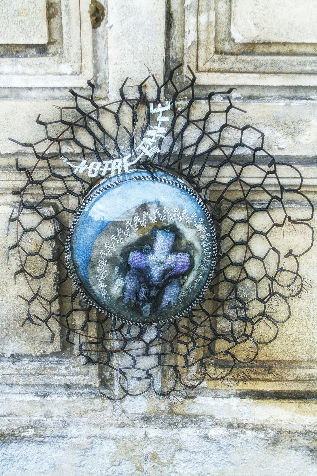 Ornate circular cross with wire mesh on a textured wall