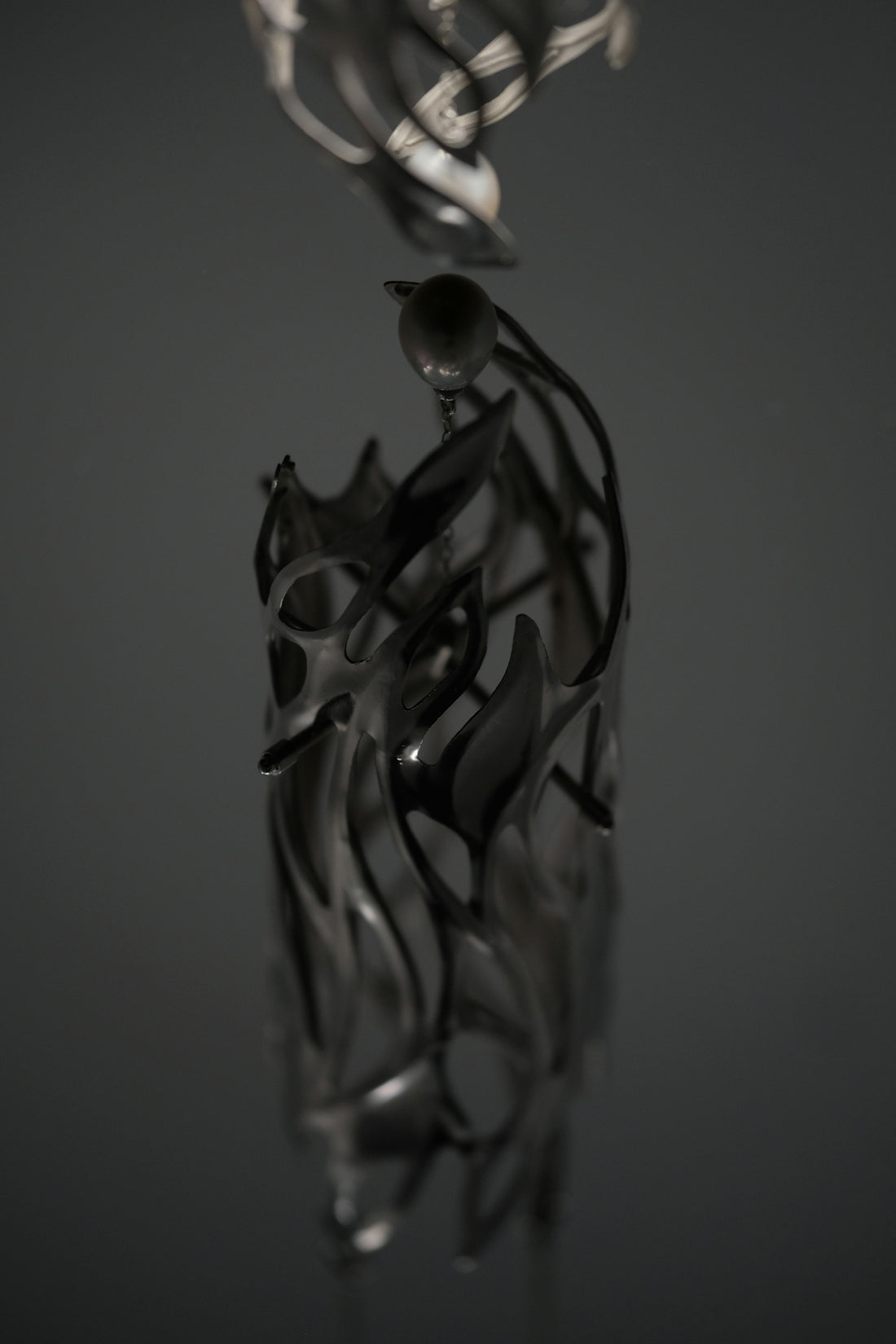 A dark metallic sculpture with organic flame-like cutouts and a single sphere