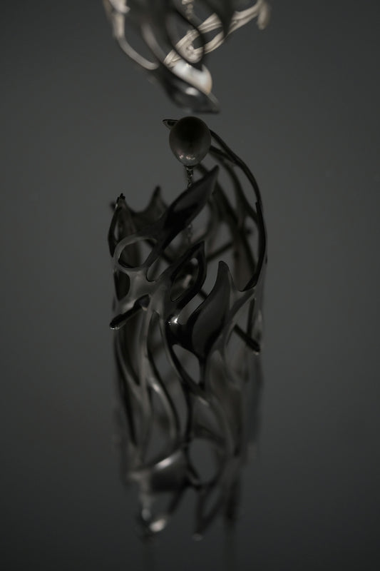 A dark metallic sculpture with organic flame-like cutouts and a single sphere